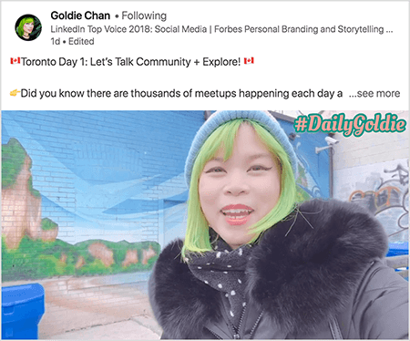 Tai yra „LinkedIn“ vaizdo įrašo, kuriame Goldie Chan dokumentuoja savo keliones, ekrano kopija. Virš vaizdo įrašo esančiame tekste sakoma „Toronto diena 1: kalbėkime apie bendruomenę + Naršyk! Ar žinojote, kad kiekvieną dieną vyksta tūkstančiai susitikimų a... Žiūrėti daugiau". Vaizdo įraše matyti, kaip Goldie priešais freską ant plytų sienos. Tapyba rodo ryškiai mėlyną dangų ir rudas uolas, padengtas ryškia žaluma. Goldie pasirodo nuo krūtinės aukštyn. Ji azijietė žaliais plaukais. Ji dėvi mėlyną megztą kepurę ir juodą parką su pūkuota apykakle. Viršutiniame dešiniajame vaizdo įrašo kampe #DailyGoldie pasirodo persikų tekstu su žaliu kontūru.
