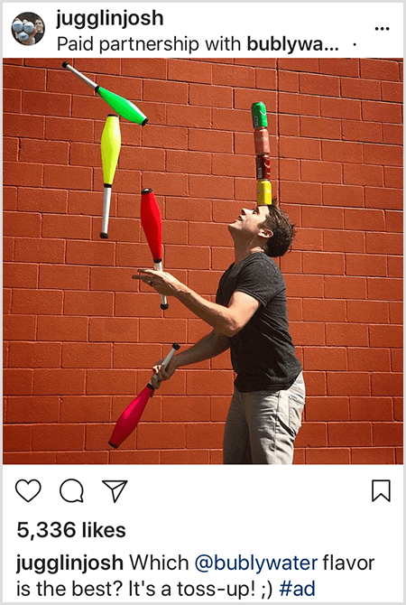 Joshas Hortonas žongliruoja klubais, kurie atitinka ant galvos sukrautų keturių „Bubly“ vandens skardinių spalvas. Fonas yra raudonų plytų siena. Nuotrauka yra Josho sukurtas skelbimas, skirtas „Bubly“ vandeniui ir paskelbtas jo „Instagram“ sklaidos kanale su aprašymu, kuris „Bubly“ vandens skonis yra geriausias? Tai mėtymasis!